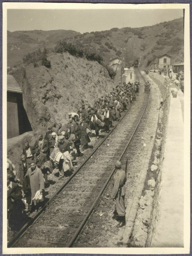 Ein altes Schwarz-Weiß-Foto zeigt eine Kolonne von Zwangsarbeitern neben einer Bahnstrecke