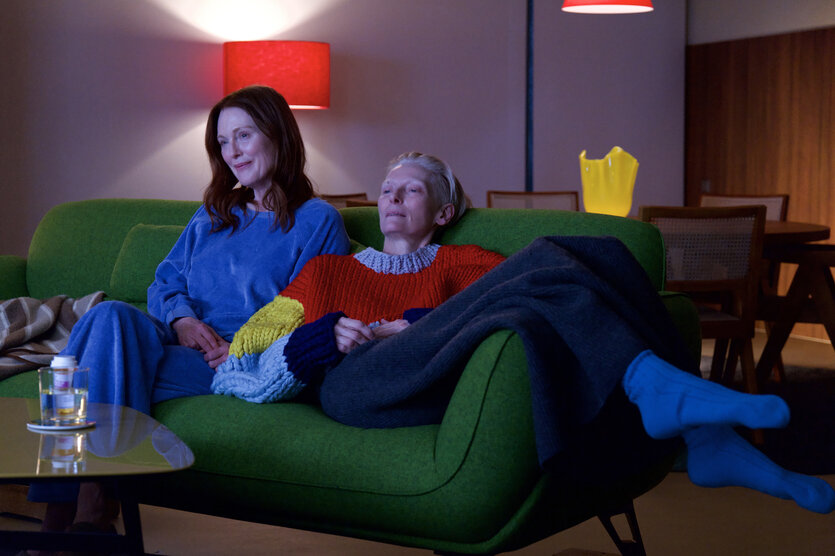 Ingrid (Julianne Moore) und Martha (Tilda Swinton) sitzen in bunter Kleidung auf einem grasgrünen Sofa.