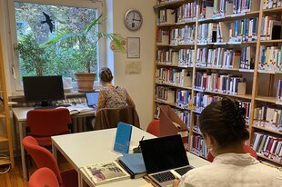 Biblithek mit Bücherregalen und zwei Frauen an Arbeitstischen