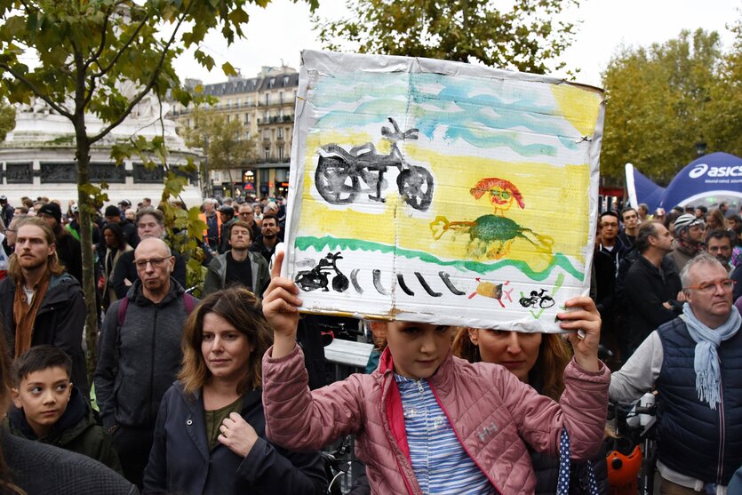 Ein Kind in demonstrierender Menge hält selbstgemaltes Bild mit Fahrrad und totem Menschen hoch