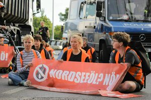 Junge Menschen in Warnwesten blockieren eine Straße in Berlin, umringt von Lastwagen und Polizeifahrzeugen halten sie auf der Straße sitzend ein Banner: Nordseeöl ? Nö !