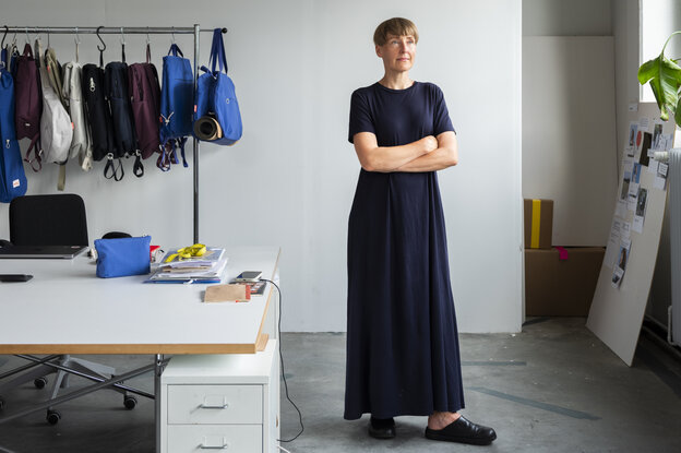 Regina Winther steht in einem langen schwarzen Kleid in ihrem weitläufigen Atelier. Hinter ihr hängen Taschen auf einem Ständer