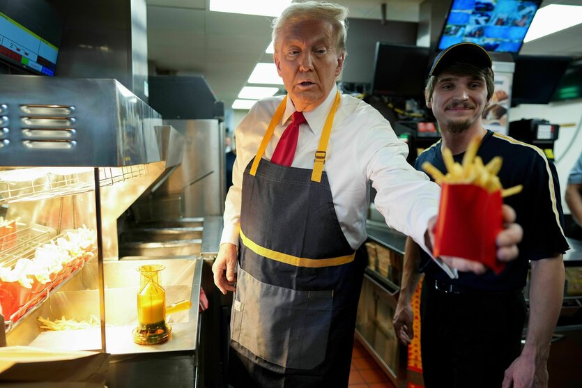 Donald Trump arbeitet bei McDonalds, er trägt eine Schürze und hat Pommes in der Hand, die er jemandem reicht