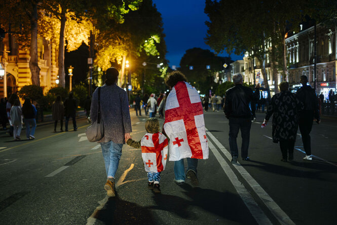 Menschen laufen am Abend eine Straße entlang, einige sind in georgischen Fahnen gewandt