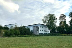 Ein grünes Feld. Im Hintergrund hinter Bäumen ein weißes Gebäude