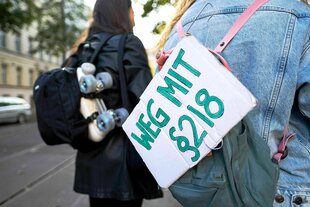 Eine Frau trägt an ihrem Rucksack ein Schild mit der Aufschrift "Weg mit Paragraph 218"