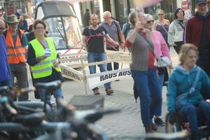 ein Mann mit einem Gestell in einer Demo, das die Ausmaße eines Autos hat