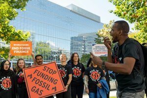 Mehrere Personen halten Schilder auf einer Demonstration, im Vordergrund ruft jemand etwas in ein Mikrofon. Auf den Schildern steht „end fossil finance“ und „stop funding fossil gas“.