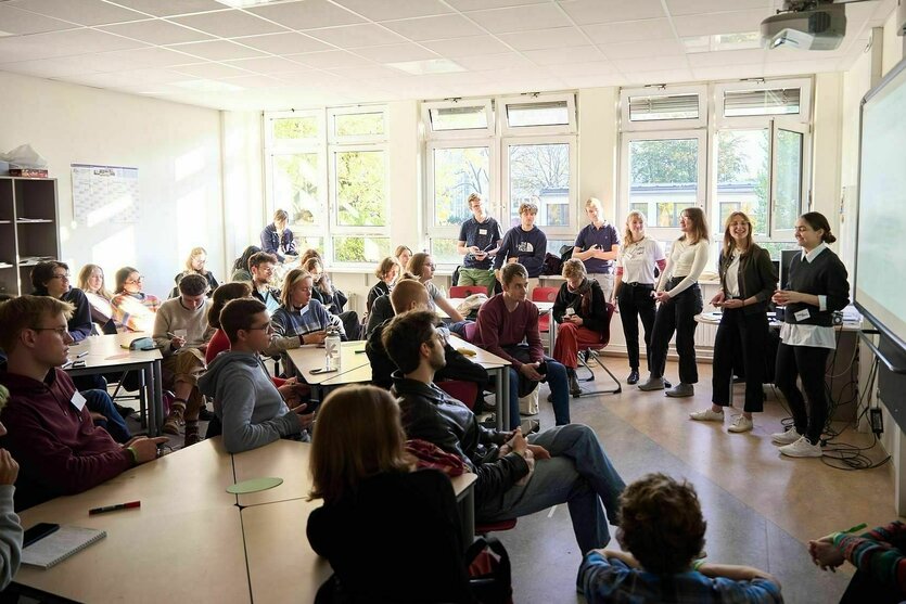 Junge Menschen sitzen in einem Seminarraum und diskutieren, es gibt eine Tafel vord er zwei jungeFrauen stehen