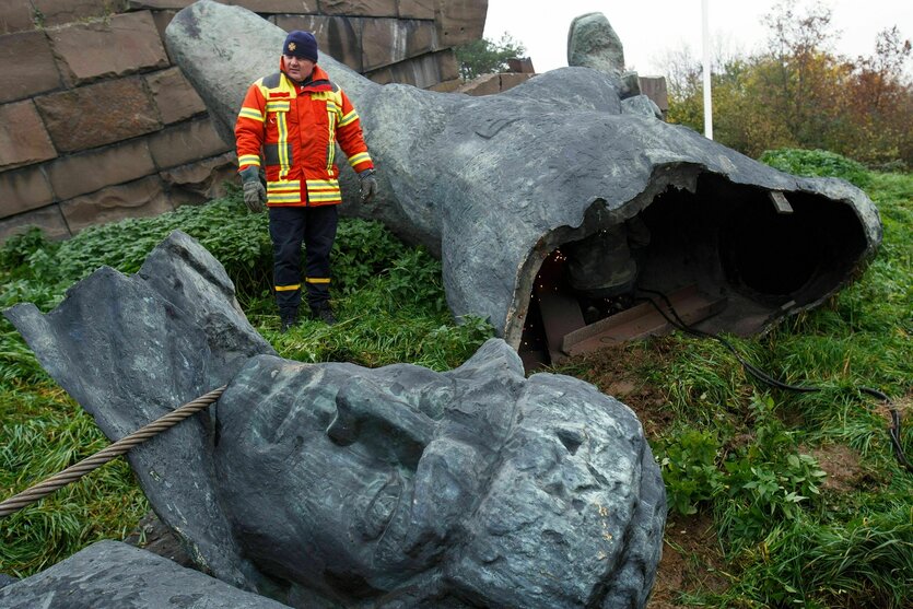 Ein Mann in Warnjacke steht zwischen den zerbrochenen Teilen eines Monuments für die sowjetischen Befreier in Uschdorod. Im Vordergrund liegt der große Kopf