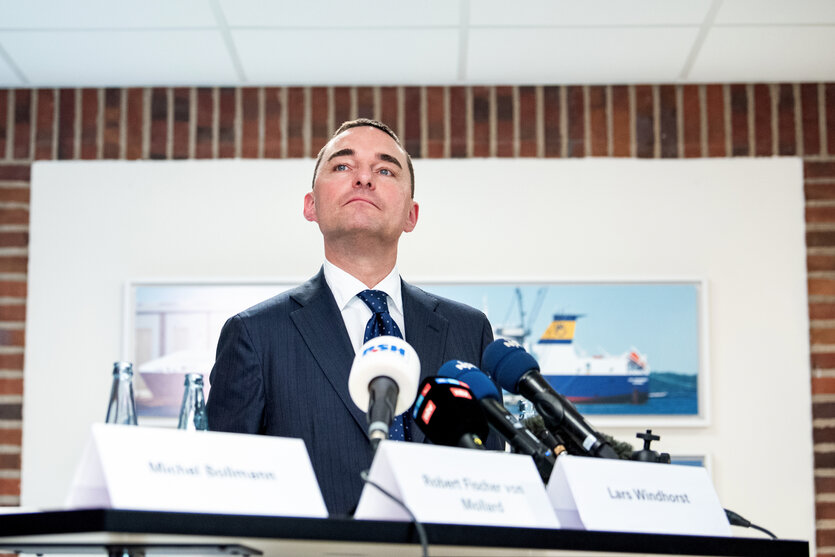 Ein Mann sitzt im Anzug am Tisch einer Pressekonferenz