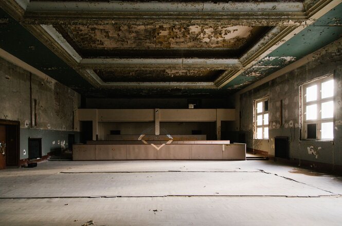 Alter Festsaal in einem verlassenen Gebäude. An der Decke ist alter Stuck in Grün- und Goldtönen zu sehen.