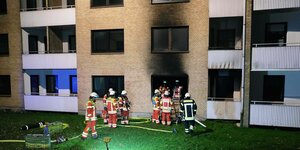 Feuerwehrleute in Scheinwerferlicht vor einer Fassade, über den Fenstern rußgeschwärzt