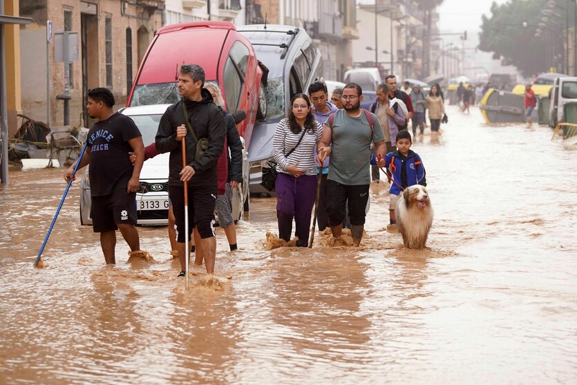 Menschen gehen durch überflutete Straßen an Autos vorbei die von den Wassermassen übereinander geschoben wurden