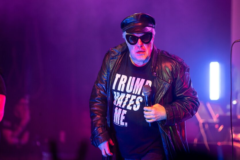 Jello Biafra mit schwarzer Kappe und Sonnenbrille, Shirt mit Aufschrift "Trump hates me" auf einer Bühne