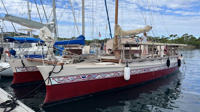 Ein bunt verzierter Katamaran mit rotem Rumpf aus Polynesien ankert im Hafen vor der Insel Porquerolles.