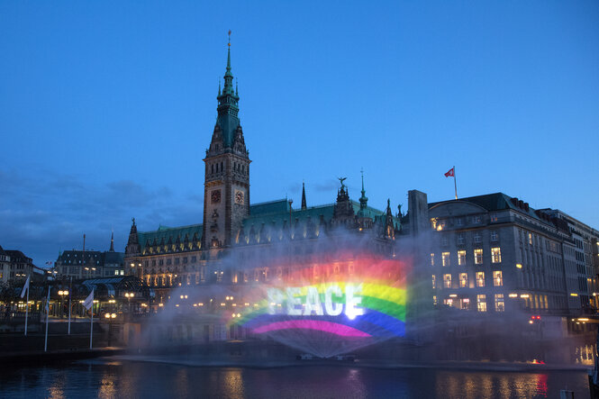 Der Schriftzug «Peace», projiziert auf eine halbrunde Wasserfontäne. Im Hintergrund ist das Hamburger Rathaus zu sehen