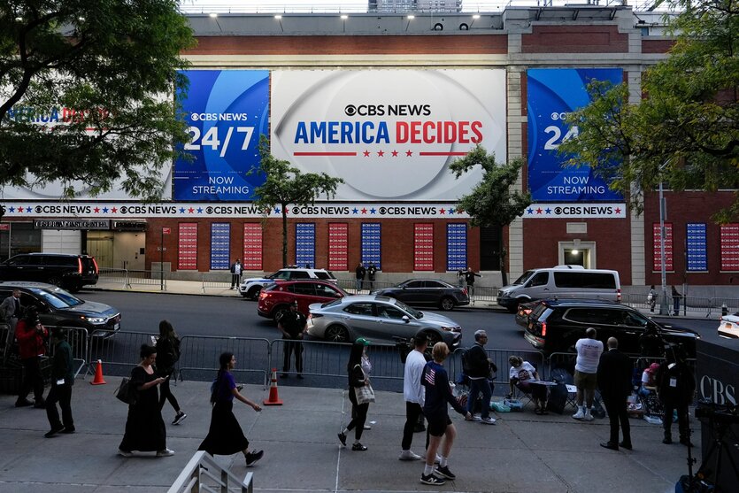 Ein Plakat von CBS News zum US-Wahlkampf hängt an einer Fassade. Menschen gehen vorbei.