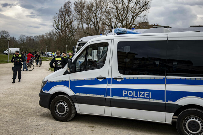 Ein großes Auto der Polizei und mehrere Polizisten stehen in einem Park