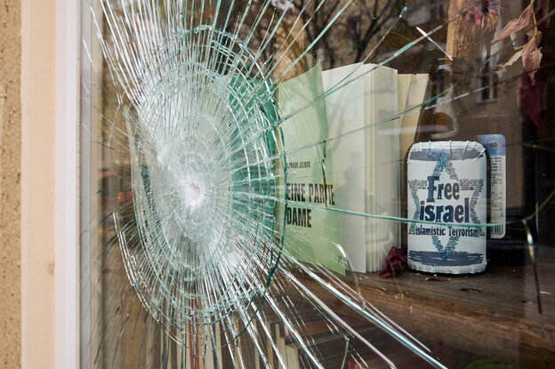 Eine geborstene Fensterscheibe mit Spuren eines Steinwurfs- hinter der Scheibe steht eine Bierflasche, aufder ein Aufkleber prant: Free Israel from Islamistic Terrorism