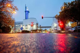 Blcik auf das VW Werk in der Abenddämmerung, das Licht einer roten Ampel spiegelt sich auf dem Asphalt, Im Hintergrund ein Turm mit dem VW Logo