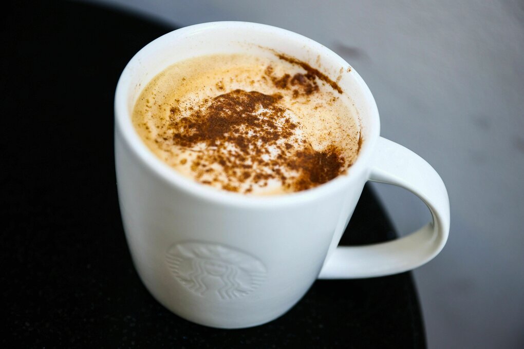 In einer weissen Tasse ein Milchkaffee mit Schlagsahne, Sirup und einer Gewürzmischung aus Dingen wie Zimt, Nelken, Piment und Muskat.