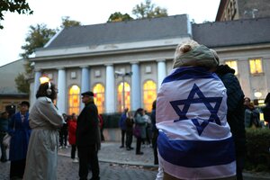 Menschen vor der Synagoge am Berliner Fraenkelufer in der Dämmerung. Eine Frau hat sich in eine Israelfahne gewickelt