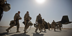 Soldaten laufen in gleißender Sonne bepackt zu einem Flugzeug
