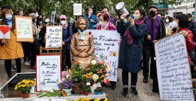 Menschen mit Protestplakaten stehen um die Trostfrauenstatue