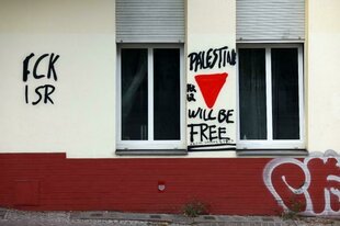 Eine Hauswand mit Graffiti "FCK ISR" und "Palestine will be free" und rotem Dreieck