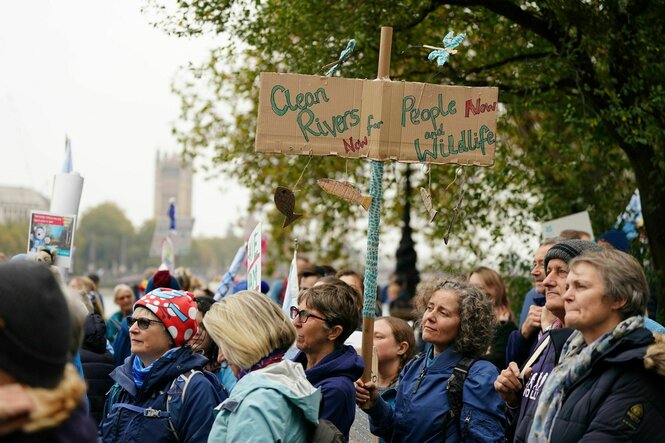 Demonstrierende; eine hält ein Pappschild mit der Aufschrift "Clean Rivers for People and Wildlife"