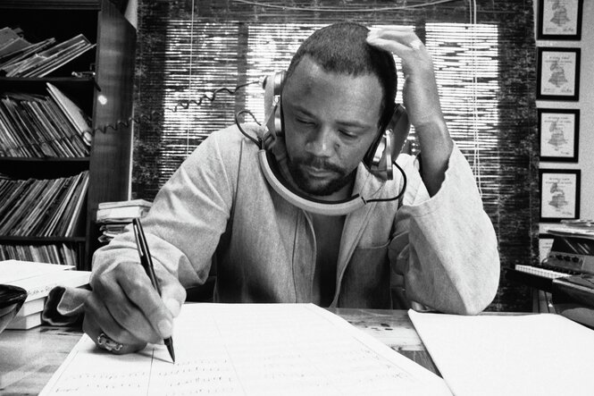 Quincy Jones sitzt an einem Tisch, Arme aufgestützt, notiert und hört Musik