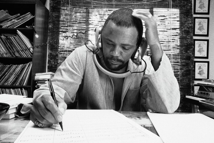 Quincy Jones sitzt an einem Tisch, Arme aufgestützt, notiert und hört Musik