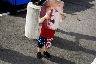 Kleiner Junge in Stars-and-Stripes-Hose mit einer Maske des kreischenden Trump