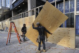 ein Mann trägt eine Holzplatte vor ein Schaufenster