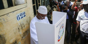 Zu sehen ist Cellou Dallein Diallo in der Wahlkabine, unter hellichtem Himmel, umgeben von Journalisten. Er trägt typische muslimische Kopfbedeckung.