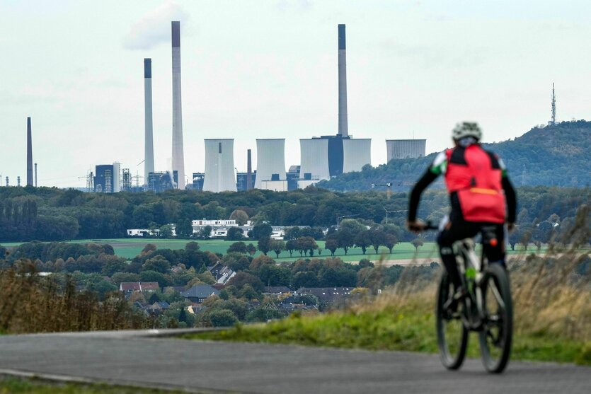 Ein Mann fährt Fahrrad in Richtung eines Kohlekraftwerks mit vielen Schloten und Kühltürmen in grüner Landschaft