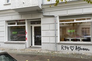 Zwei Schaufenster mit dem grünen großen Schriftzug MUT: die Beratungsstelle von MUT in der Rigaer Straße in Friedrichshain von außen gesehen