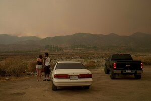 Zwei Personen stehen neben Fahrzeugen und schauen auf einen Waldbrand.