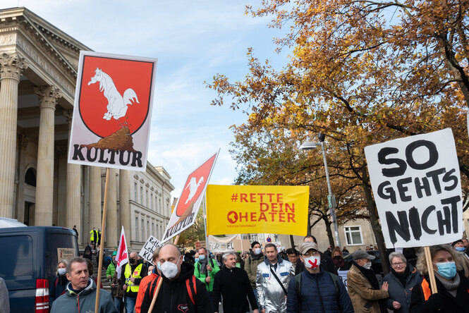 Auf einer Demonstration wird ein Schild mit dem niedersächsischen Wappen hochgehalten sowie ein Banner, auf dem steht: #rettedeintheater