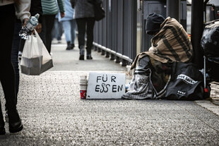 Ein Obdachloser sitzt auf der Strasse mit einem Schild "FÜR ESSEN"