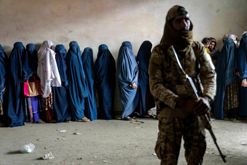 Frauen in Burkas werden von einem Taliban mit Maschinengewehr bewacht