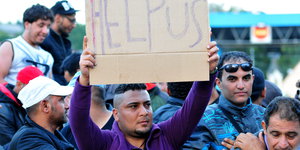 Ein Mann hält ein Schild mit der Aufschrift "Help us".