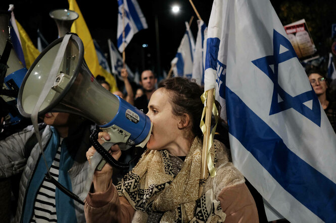 Eine Frau mit Megaphon und israelischer Fahne demonstriert