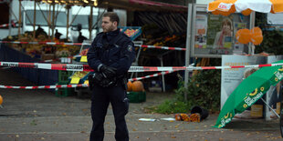 Ein Polizist auf einem Wochenmarkt. Im Hintergrund Absperrungen.