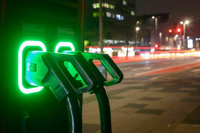 Zwei grün-leuchtende Ladensäulen für Elektroautos nachts am Straßenrand