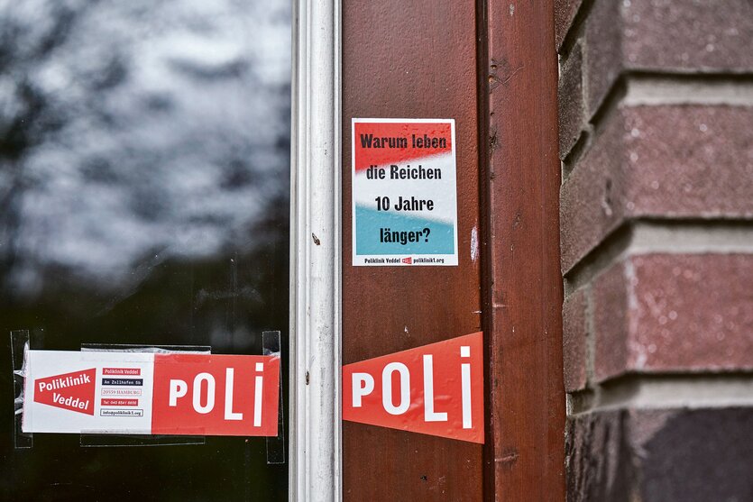 Fenster der Hamburger Poliklinik Veddel, die Vorbild für die Gesundheitsstrategie der Bremer Linken ist. Auf dem Rahmen kleben Aufkleber mit der Aufschrift "Poli" sowie "Warum leben die Reichen zehn Jahre länger?"