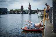 Ein Mann turnt an einer Treppe an der Spree in der Nähe der Oberbaumbrücke, ein weiterer steht am Ufer