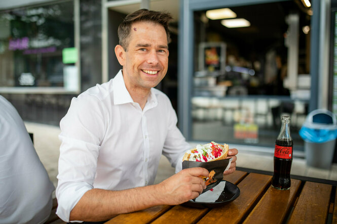 Christoph Troßbach am Tisch eines Dönerladens mit weißem Hemd und Döner in der Hand