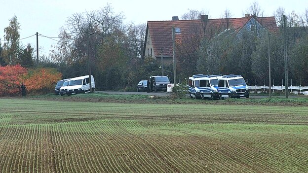 Neblige Herbst-Stimmung auf dem Land, Polizeiautos stehen am Rande eines Ackers, im Hintergrund ist ein Haus mit Zaun umgeben von Bäumen zu sehen